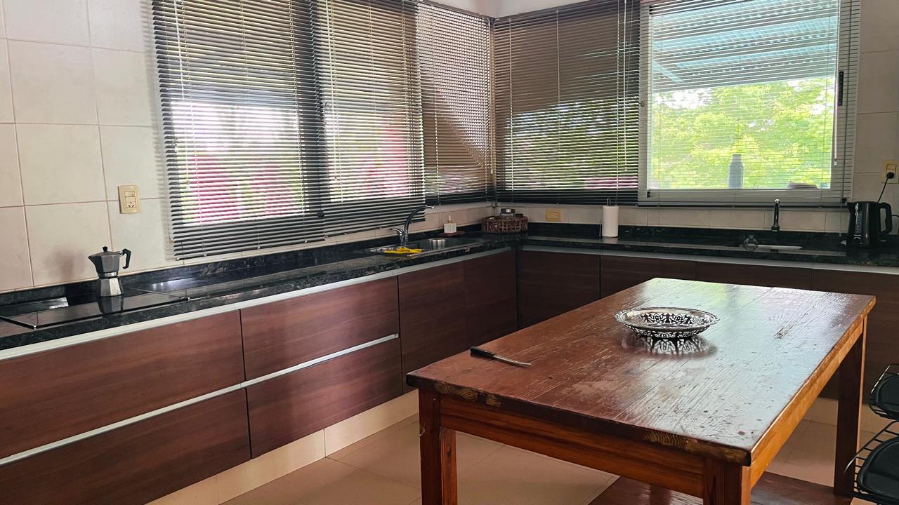 Cocina con amplias mesadas, ventanas y mesa central de madera